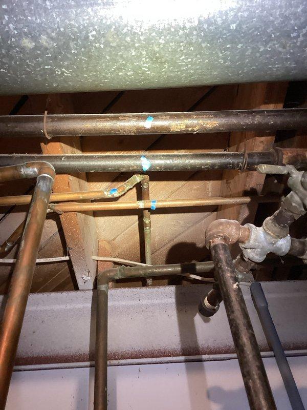 Performed comprehensive inspection of boiler system and associated piping infrastructure in attic space. Documented existing copper supply lines and PVC condensate drainage system, noting multiple connection points marked for reference. Evaluated condition of horizontal pipe runs supported by wooden joists, including sections with reflective insulation wrapping. Assessed aging metal piping showing surface oxidation and verified structural support integrity throughout the installation. Inspected complex PVC joint configurations and confirmed proper drainage routing from boiler system.
