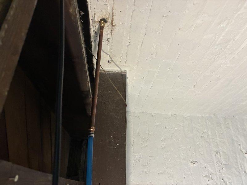 Conducted comprehensive plumbing fixture assessment in utility area with aging infrastructure. Inspected copper and PVC water supply lines at wall junction, evaluated shut-off valve functionality and condition, and documented deteriorated wooden framing with moisture damage and biological growth around plumbing penetrations. Photographed existing conditions including painted surface deterioration, pipe routing configuration, and valve accessibility for fixture replacement estimate preparation.