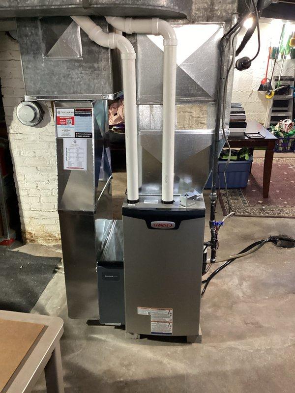 Completed installation of new Lennox high-efficiency furnace in basement location. Installed unit on concrete pad with proper leveling, connected white PVC intake and exhaust venting vertically through structure, and secured black flexible condensate drain lines to underside of equipment with metal clamps and white plastic fittings for proper drainage. Verified all connections, tested system operation, and ensured compliance with manufacturer specifications.