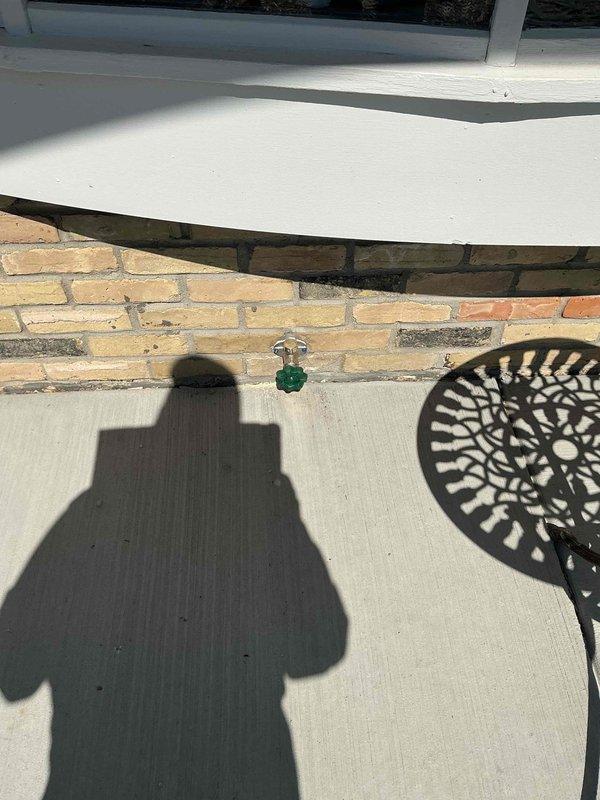 Installed new exterior water service including hose bib with green handle valve mounted on brick exterior wall of residence. Completed interior rough-in plumbing work in basement area, installing copper water supply lines with appropriate fittings, elbows, and connections through floor joists to supply the new exterior fixture.