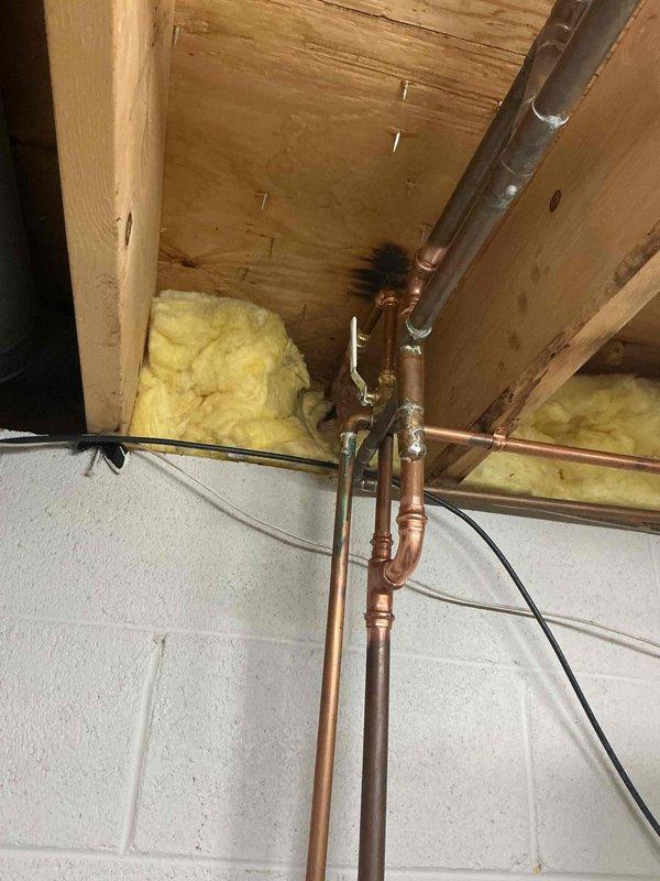 Installed new exterior water service including hose bib with green handle valve mounted on brick exterior wall of residence. Completed interior rough-in plumbing work in basement area, installing copper water supply lines with appropriate fittings, elbows, and connections through floor joists to supply the new exterior fixture.
