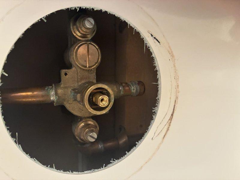 Accessed shower valve assembly through wall opening to address plumbing concerns. Removed deteriorated copper piping showing significant green patina and corrosion from water exposure. Replaced aging valve mechanism and brass fittings with new components. Installed new brushed stainless steel trim plate and valve assembly, ensuring proper alignment and secure mounting. Tested system for proper water flow and verified no leaks present upon completion.