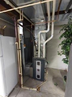 Completed routine maintenance and inspection of residential gas furnace system in basement mechanical room. Verified proper operation of heating unit, inspected all ductwork connections, examined refrigerant lines and plumbing connections for leaks or damage, and confirmed electrical components and control panel functioning correctly. All equipment found to be in good working condition with proper airflow through white supply ductwork and secure mounting of furnace cabinet.