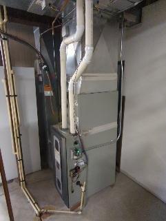 Completed routine maintenance and inspection of residential gas furnace system in basement mechanical room. Verified proper operation of heating unit, inspected all ductwork connections, examined refrigerant lines and plumbing connections for leaks or damage, and confirmed electrical components and control panel functioning correctly. All equipment found to be in good working condition with proper airflow through white supply ductwork and secure mounting of furnace cabinet.