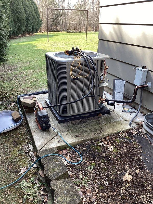 Completed installation of new residential central air conditioning system including outdoor condensing unit and evaporator coil. Mounted gray condensing unit on concrete pad with proper clearances from building structure, installed gray electrical disconnect box on exterior wall per code requirements, and ran refrigerant line set with black foam insulation from outdoor unit through wall penetration to indoor coil location. Connected copper refrigerant lines, electrical wiring, and condensate drain line to complete system integration. Performed vacuum and pressure testing of refrigerant circuit using diagnostic equipment to verify system integrity prior to charging. Successfully commissioned system with all components operating within manufacturer specifications.