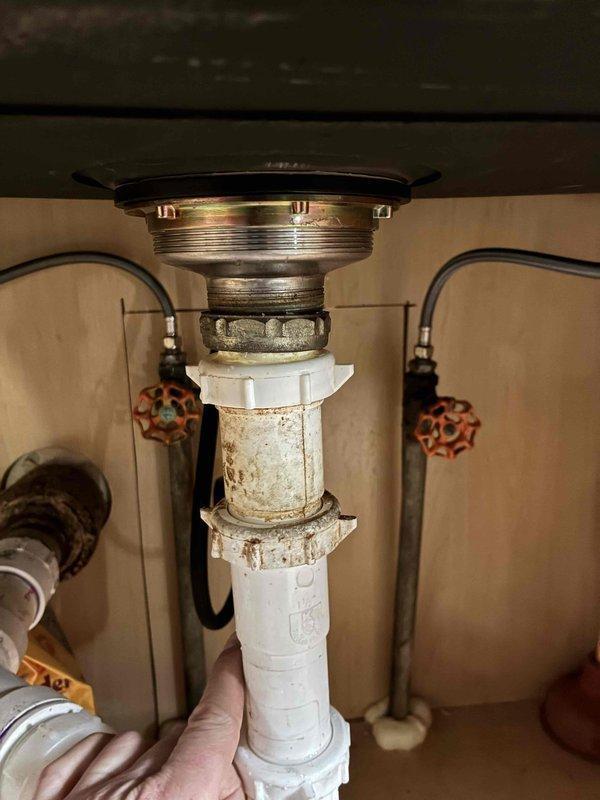 Responded to under-sink plumbing issue involving corroded and deteriorating PVC drain pipe assembly beneath kitchen sink. Upon inspection, identified significant discoloration and corrosion on the vertical drain pipe connecting to the garbage disposal unit, with brownish staining indicating water damage and material breakdown. Replaced the compromised white PVC drain assembly with new components, ensuring proper connection to the existing garbage disposal mounting flange and P-trap configuration. Verified all threaded connections and coupling nuts were properly sealed to prevent future leaks. Tested the complete drain system for proper water flow and confirmed no leaks at connection points.