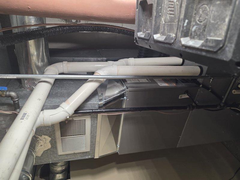 # HVAC Install - A/C & Coil

Completed installation of new air conditioning system including outdoor condensing unit and indoor evaporator coil. Installed outdoor unit on textured concrete pad with proper leveling and positioning adjacent to building structure. Connected refrigerant lines between outdoor condenser and indoor coil using appropriate line sets with proper insulation. Established PVC condensate drainage system with multiple connection points and proper pitch for efficient water removal from evaporator coil. Integrated new coil assembly into existing ductwork infrastructure within mechanical space, ensuring proper airflow alignment with return air plenum and filter access. Performed vacuum and pressure testing of refrigerant system using digital manifold gauges to verify system integrity and absence of leaks. Charged system with manufacturer-specified refrigerant to proper levels based on line length and ambient conditions. Verified electrical connections at both indoor and