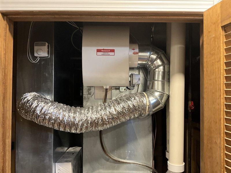 Completed HVAC system replacement including installation of new Lennox outdoor condensing unit positioned on concrete pad with updated landscaping clearance. Interior components include new air handler with integrated Honeywell humidifier system, metallic ductwork with flexible connections, condensate drain piping, and associated electrical controls mounted in utility closet. All equipment installed per manufacturer specifications with proper airflow configuration and drainage connections.