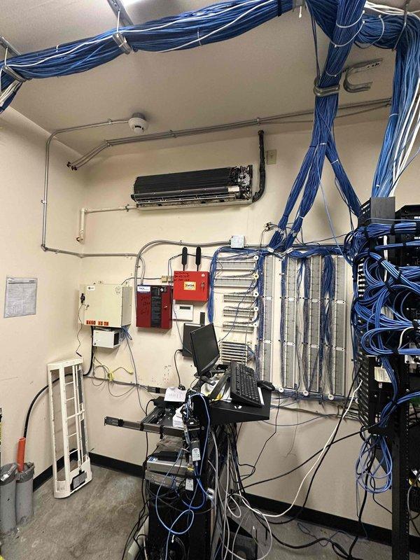 Completed commercial HVAC estimate for mini-split system installation in equipment room with existing data infrastructure and cable management systems. Assessed exterior wall-mounted Sanyo condenser unit and interior mounting requirements, evaluating electrical conduit routing, refrigerant line placement, and condensate drainage integration with existing building systems.