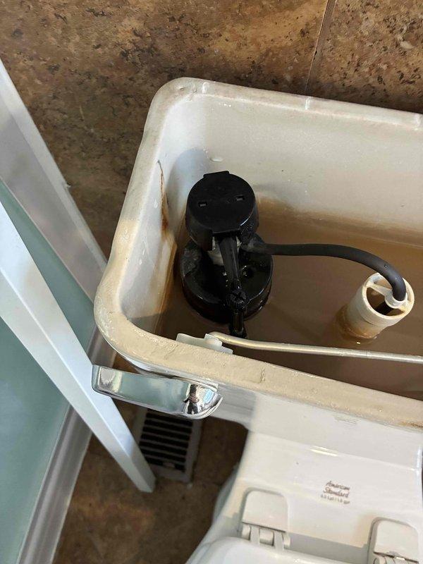 Completed comprehensive plumbing inspection of residential bathroom toilet system. Examined water supply line connections, flush valve assembly, and internal tank components, documenting discolored water indicating mineral deposits and hard water conditions requiring attention. Assessed floor-mounted plumbing fixtures, supply line integrity, and overall system functionality, noting aging components with mineral staining throughout tank interior.