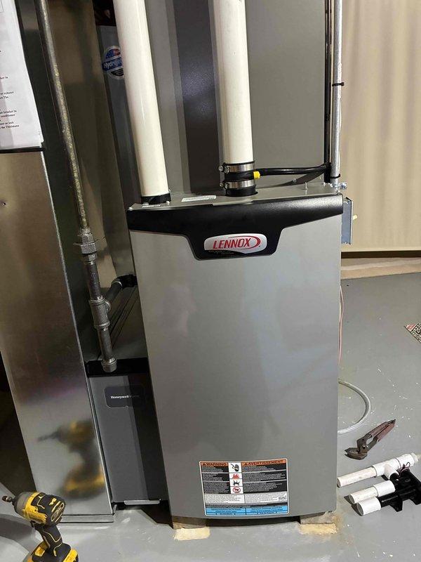 Completed installation of Lennox furnace unit in residential basement utility space. Unit was positioned on concrete floor with protective foam padding, connected to existing ductwork system including metal supply ducts and white PVC condensate drain lines. During installation, identified existing water infiltration issues at wall-to-floor junction near piping penetrations, evidenced by discoloration and moisture damage to substrate materials. All mechanical connections, venting, and drain lines were properly secured with appropriate mounting brackets and fittings to ensure code-compliant operation.