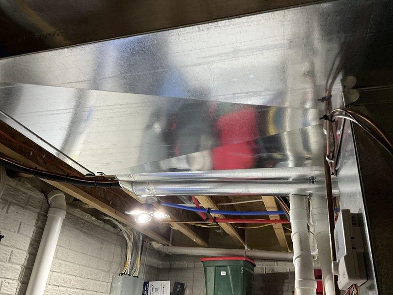 Completed HVAC ductwork installation in basement utility space, including installation of large rectangular metal supply plenum with galvanized steel construction. The new ductwork was properly suspended from floor joists and integrated with existing electrical wiring and PVC plumbing systems while maintaining proper clearances and code compliance.