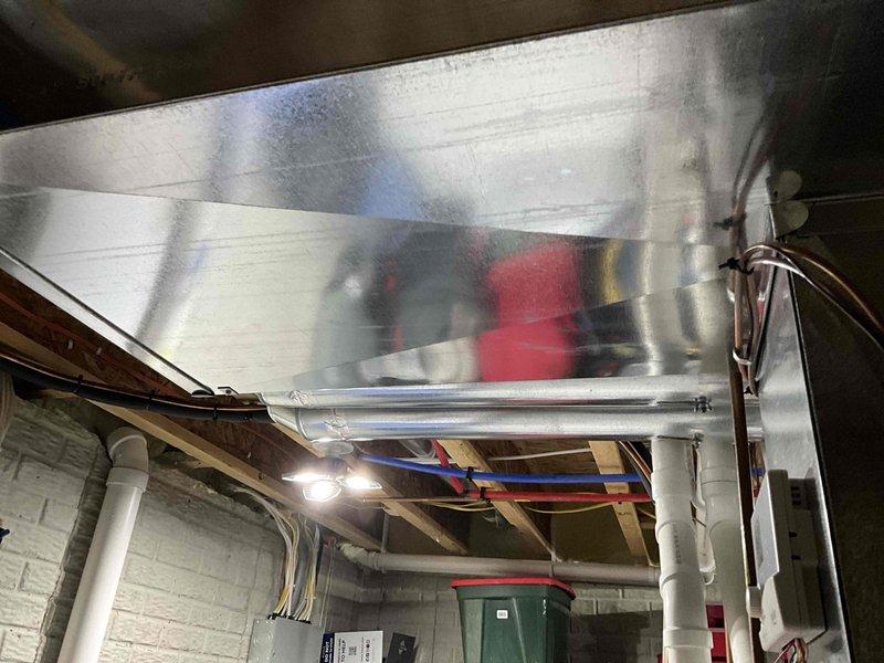Completed HVAC ductwork installation in basement utility space, including installation of large rectangular metal supply plenum with galvanized steel construction. The new ductwork was properly suspended from floor joists and integrated with existing electrical wiring and PVC plumbing systems while maintaining proper clearances and code compliance.