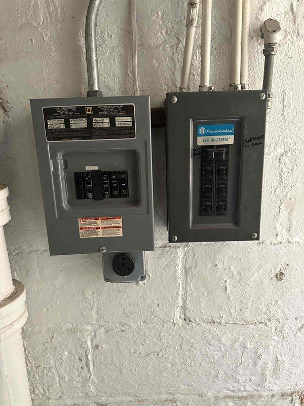 Completed comprehensive HVAC system replacement estimate for residential property with aging outdoor condensing unit and existing electrical infrastructure. Assessed current light green/turquoise condenser unit positioned on concrete pad against exterior wall, evaluated electrical panel configuration including Square D and Techni-Center breaker boxes mounted in utility area, and documented existing electrical capacity and conduit routing to determine replacement system requirements and installation specifications.