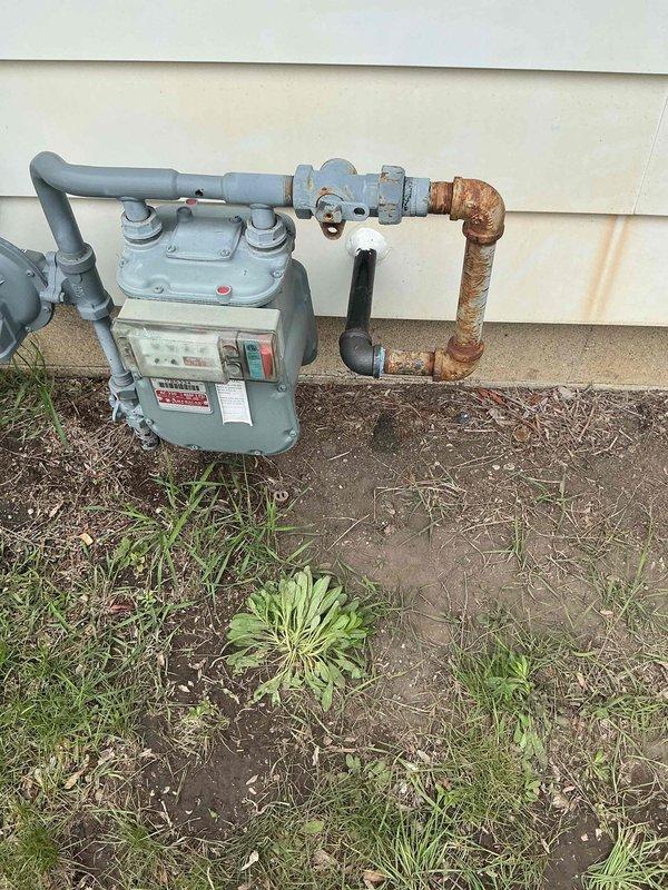 Completed installation of tankless water heater system including assessment of existing natural gas supply infrastructure and utility connections. Documented pre-installation conditions showing gas meter assembly with corroded piping sections requiring evaluation for adequate gas supply capacity. Performed installation work in basement utility area involving structural access and integration with existing plumbing infrastructure to accommodate new tankless unit.