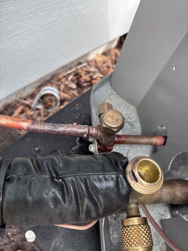 # HVAC Refrigerant Line Service and Inspection

Performed warranty service on aging HVAC system with heavily corroded copper refrigerant lines showing significant oxidation and weathering. Accessed refrigerant service ports to conduct system diagnostics and pressure testing. Inspected brass service valves and charging ports, which displayed extensive corrosion consistent with prolonged outdoor exposure. 

Evaluated sight glass component showing oil residue accumulation, indicating potential refrigerant flow concerns. Assessed condition of refrigerant line connections and fittings at exterior equipment location near foundation. System components required careful handling due to advanced deterioration of copper piping and brass fittings. Completed thorough inspection of refrigerant circuit integrity and documented equipment condition for warranty claim processing.