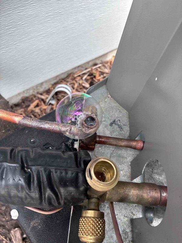 # HVAC Refrigerant Line Service and Inspection

Performed warranty service on aging HVAC system with heavily corroded copper refrigerant lines showing significant oxidation and weathering. Accessed refrigerant service ports to conduct system diagnostics and pressure testing. Inspected brass service valves and charging ports, which displayed extensive corrosion consistent with prolonged outdoor exposure. 

Evaluated sight glass component showing oil residue accumulation, indicating potential refrigerant flow concerns. Assessed condition of refrigerant line connections and fittings at exterior equipment location near foundation. System components required careful handling due to advanced deterioration of copper piping and brass fittings. Completed thorough inspection of refrigerant circuit integrity and documented equipment condition for warranty claim processing.