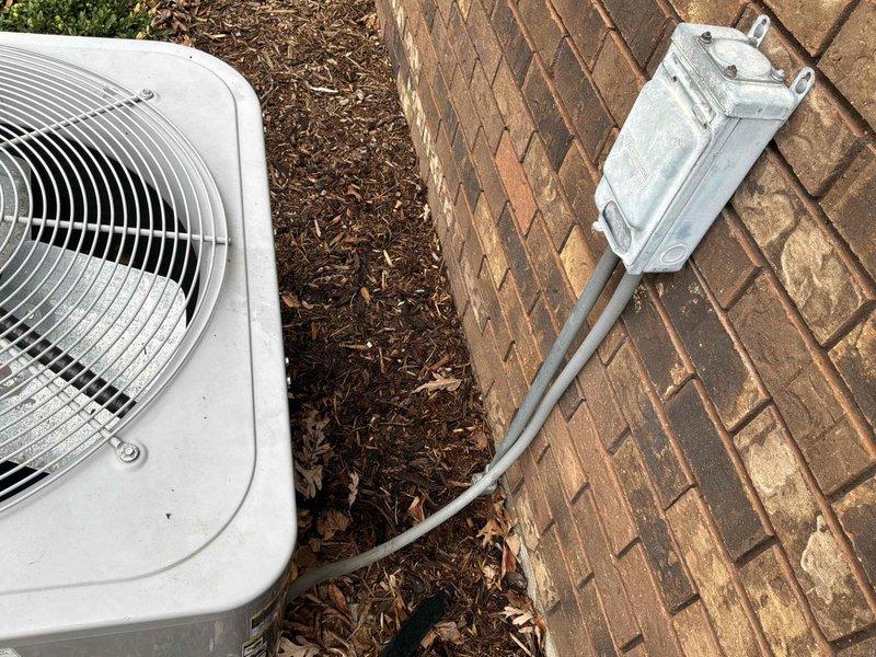 Conducted comprehensive site evaluation for complete HVAC system replacement at residential property. Assessed existing outdoor condensing unit positioned against brick exterior wall, documented current equipment configuration including electrical disconnect box, conduit routing, and refrigerant line placement. Evaluated installation area conditions including mulch bedding, patio brick surface, and clearance requirements for new equipment placement. Photographed existing unit with protective cover in place and exposed condenser unit to document current system specifications, mounting location, and utility connections. Provided detailed replacement estimate covering removal of existing equipment and installation of new high-efficiency HVAC system with properly sized condensing unit, updated electrical connections, and compliant refrigerant line routing across herringbone brick patio surface.