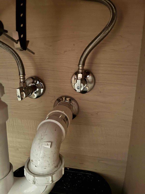 Completed installation of chrome cross-handle faucet assembly on bathroom sink with beige composite countertop. Connected new braided flexible supply lines from wall-mounted shut-off valves to faucet, ensuring proper water flow to fixture. Verified all connections are secure, tested for leaks, and confirmed proper drainage through existing white PVC P-trap assembly.