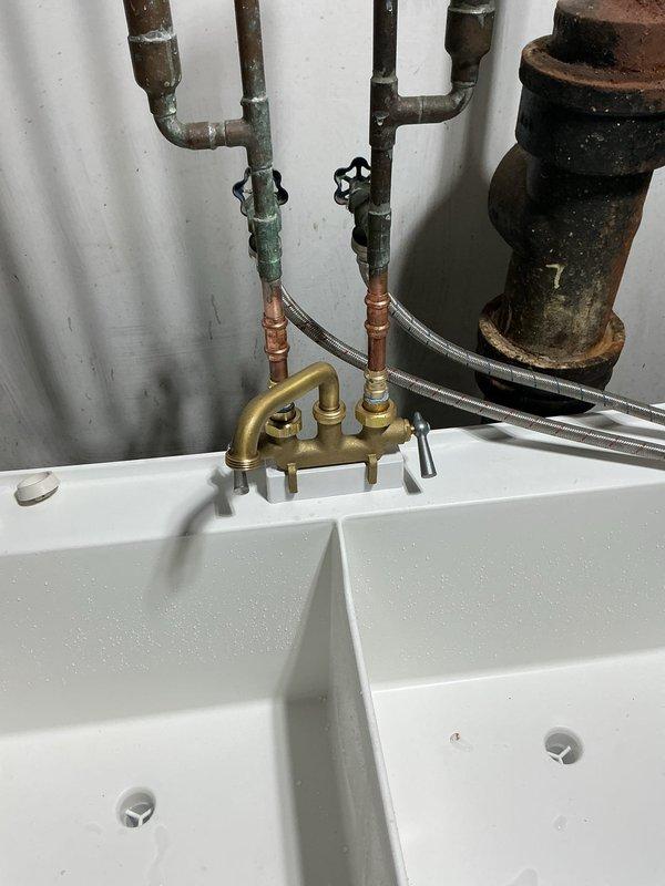 Responded to emergency call for broken pipe at utility sink installation in basement mechanical room. Upon arrival, found compromised section of aged galvanized supply piping showing severe corrosion and active water damage to surrounding concrete floor area. 

Shut off main water supply and assessed full extent of plumbing system. Identified failed connection point at brass manifold assembly serving dual-compartment utility sink. Removed deteriorated galvanized pipe sections and corroded fittings that had reached end of service life. 

Installed new brass manifold with multiple connection points and control valves to properly distribute water supply. Replaced compromised piping with new copper supply lines and brass fittings to ensure code-compliant installation. Connected flexible braided supply hoses to provide reliable water delivery to both sink compartments. Installed shut-off valves on vertical supply lines for future maintenance access.

Pressure tested all new connections to v