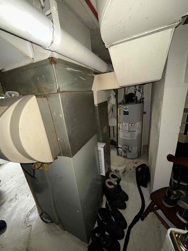 Conducted comprehensive assessment of existing HVAC system and water heater located in basement mechanical room for equipment replacement estimate. Evaluated aging furnace or air handler unit with visible rust staining on metal ductwork and casings, indicating advanced wear and potential compromised system integrity. Documented current system configuration including existing ductwork layout, white insulated refrigerant lines, cylindrical humidifier or air cleaner attachment, and overall mechanical room accessibility for replacement equipment installation. Assessed utility room dimensions and clearances to determine appropriate replacement unit sizing and installation requirements. Provided detailed replacement recommendations and equipment specifications for new HVAC system installation.
