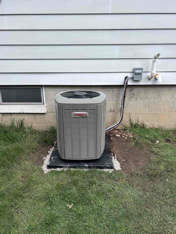 Completed installation of new Lennox air conditioning condenser unit with matching evaporator coil system. Positioned outdoor condenser on rubber equipment pad with concrete foundation base, ensuring proper clearance from building structure for optimal airflow and serviceability. Ran refrigerant line set with black foam insulation from outdoor unit to indoor coil location, securing copper lines along exterior wall. Installed PVC condensate drain line routing from indoor coil to exterior discharge point. Verified all electrical connections, refrigerant charge levels, and system pressures meet manufacturer specifications. Tested complete system operation including compressor function, fan motor performance, and airflow delivery to confirm proper cooling cycle and temperature differential across coil.