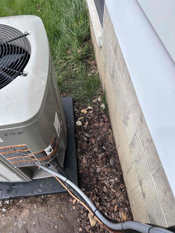 Completed installation of new Lennox air conditioning condenser unit with matching evaporator coil system. Positioned outdoor condenser on rubber equipment pad with concrete foundation base, ensuring proper clearance from building structure for optimal airflow and serviceability. Ran refrigerant line set with black foam insulation from outdoor unit to indoor coil location, securing copper lines along exterior wall. Installed PVC condensate drain line routing from indoor coil to exterior discharge point. Verified all electrical connections, refrigerant charge levels, and system pressures meet manufacturer specifications. Tested complete system operation including compressor function, fan motor performance, and airflow delivery to confirm proper cooling cycle and temperature differential across coil.