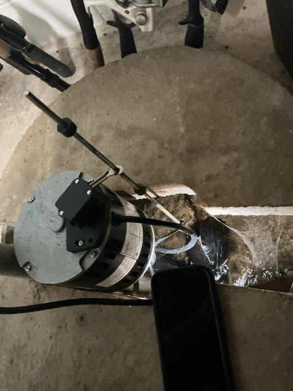 Performed inspection and assessment of existing sump pump system in basement utility area. Documented current condition of pump assembly, discharge piping, and basin installation. Observed evidence of previous water accumulation and moisture issues based on floor staining patterns. Verified sump pump operation, electrical connections, and discharge pipe mounting. Checked basin positioning within floor pit and confirmed proper drainage configuration. Photographed system components including pump mechanism, vertical discharge assembly with wall-mounted brackets, and associated plumbing connections for service records.