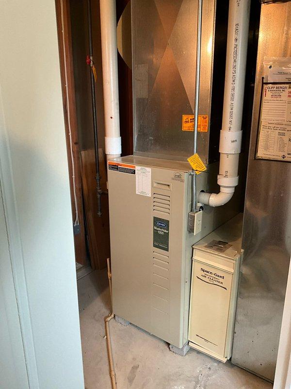 Completed comprehensive HVAC system evaluation for equipment replacement estimate. Assessed existing Carrier furnace unit in basement utility area and outdoor air conditioning condenser unit, documenting current equipment specifications, installation conditions, and system configuration including copper refrigerant lines, PVC condensate drainage, and venting components to provide accurate replacement recommendations and sizing requirements.