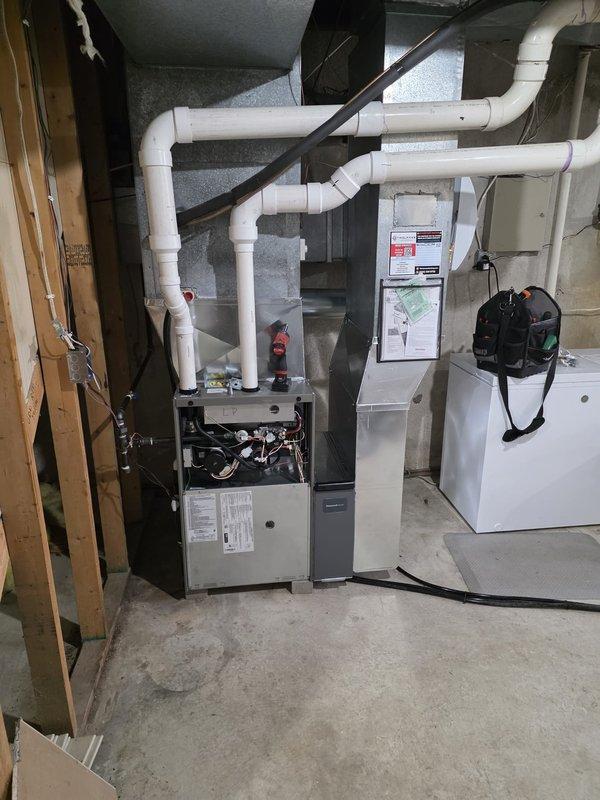 Completed full furnace installation in basement utility area. New gas furnace unit was installed with proper venting configuration using white PVC piping system, connected to existing ductwork distribution system with black metal supply plenum. All internal components including blower motor, control circuitry, capacitors, and burner assembly were installed and wired according to manufacturer specifications. Unit was tested and verified operational.