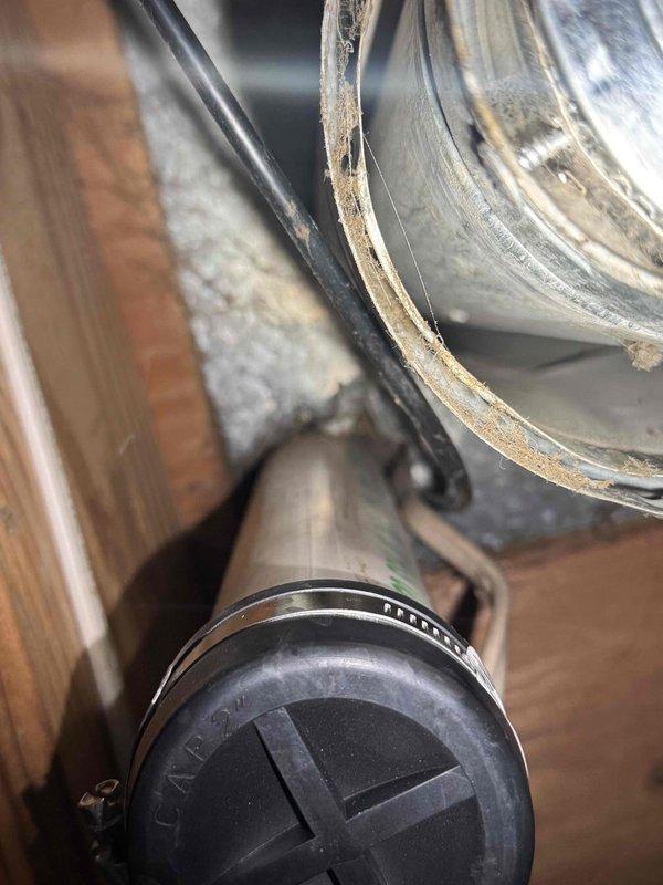 Performed AC system startup on EL18 unit with S40 thermostat, confirming disconnect switch on, service valves open, breaker energized, and system operational. Investigated customer concern regarding furnace vent pipe leaking water into basement during heavy rain events. Inspected ductwork connections and vent termination components in attic space, documenting condition of flexible ductwork, metal duct connections, and end cap assembly with visible dust accumulation and potential weatherproofing concerns.