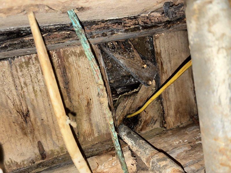 Responded to commercial property for water leak originating from first floor and extending down to basement level. Upon inspection, discovered deteriorated wooden structural members with significant moisture damage and rot in the affected area, evidenced by heavy black staining on horizontal and vertical support beams. Located and repaired the source of the leak involving aged copper piping showing green patina oxidation. Addressed secondary plumbing issue involving PVC drainage system with corroded metal collar fitting causing rust staining on surrounding tiled surface. Completed installation of new water line connection for refrigerator appliance as requested.