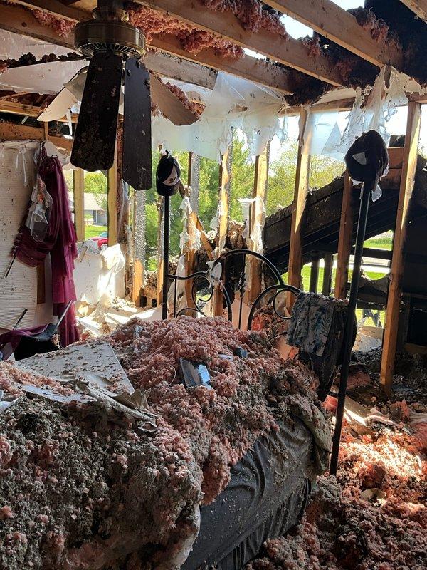 Conducted comprehensive restoration site walk-through and documented property conditions following fire damage. Photographed intact bathroom area showing functional fixtures and existing HVAC considerations, as well as severely fire-damaged structure with compromised roof, exposed framing, and extensive fire retardant contamination requiring full system assessment for restoration planning.