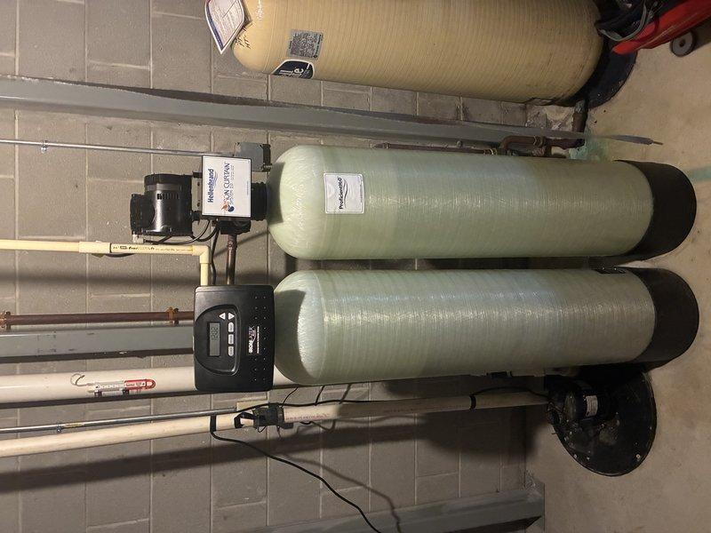 Completed installation of dual-tank water treatment and filtration system in residential basement utility area. System includes two fiberglass filtration tanks with digital control valve, integrated with existing plumbing infrastructure and water heater. All piping connections, electrical components, and control panel successfully installed and tested for proper operation.