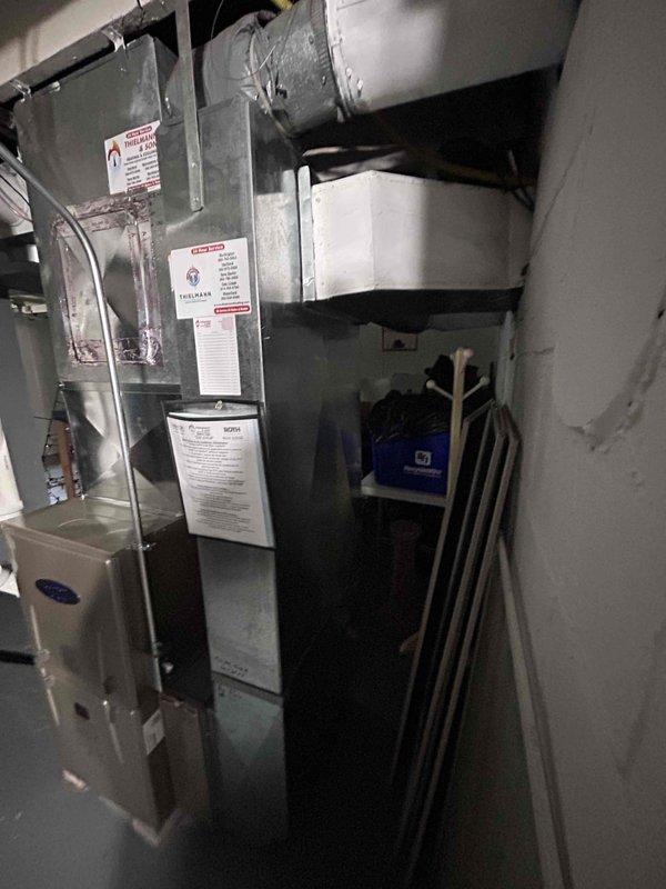 Completed installation of new furnace and humidifier system in residential basement location. Installed gray metal vertical cabinet-style furnace unit with associated ductwork connections, routing large supply and return ducts through exposed ceiling joists. Connected humidifier equipment to system, with PVC condensate drainage piping staged for final connection. All equipment properly positioned on concrete floor, ductwork secured to ceiling structure with appropriate hangers, and system prepared for startup and commissioning.
