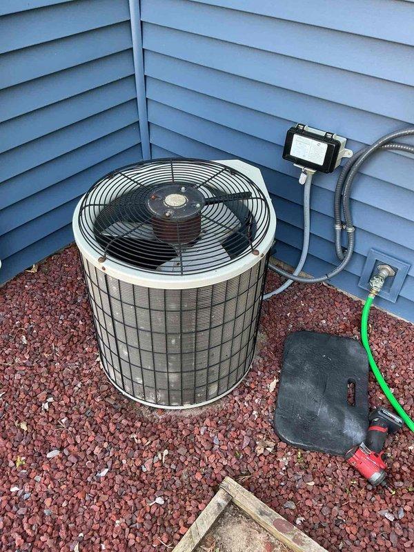 Conducted comprehensive site evaluation for complete HVAC system replacement. Assessed existing outdoor condenser unit with cylindrical cage housing positioned on gravel pad against building exterior, noting metallic conduit connections and control module mounting. Inspected basement furnace system with green cabinet, exposed blower assembly, and PVC venting configuration. Documented current equipment specifications, electrical connections, refrigerant line routing, and ductwork layout to provide accurate replacement estimate for both heating and cooling components.