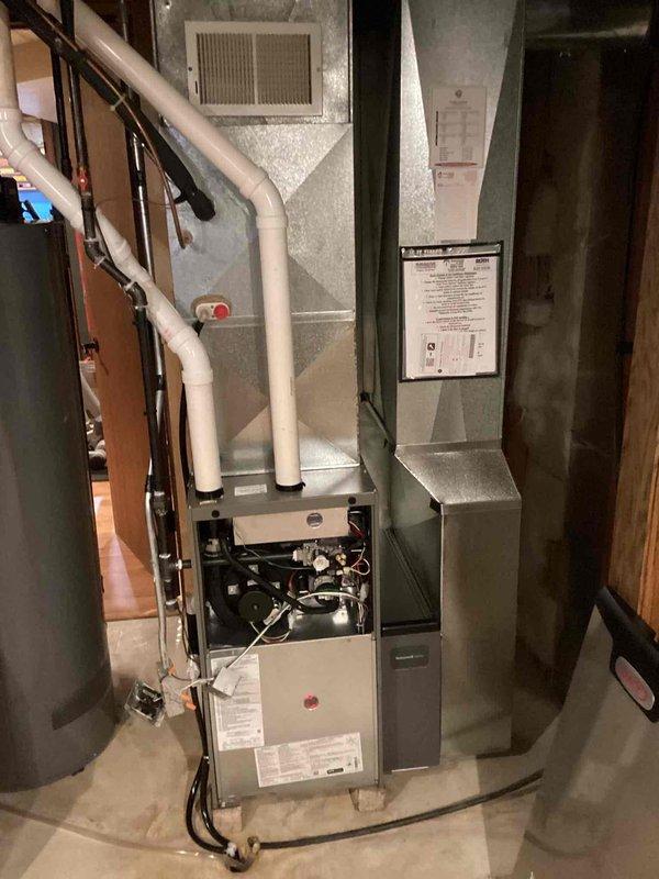Conducted comprehensive site evaluation for complete HVAC system replacement. Assessed existing outdoor condenser unit with cylindrical cage housing positioned on gravel pad against building exterior, noting metallic conduit connections and control module mounting. Inspected basement furnace system with green cabinet, exposed blower assembly, and PVC venting configuration. Documented current equipment specifications, electrical connections, refrigerant line routing, and ductwork layout to provide accurate replacement estimate for both heating and cooling components.