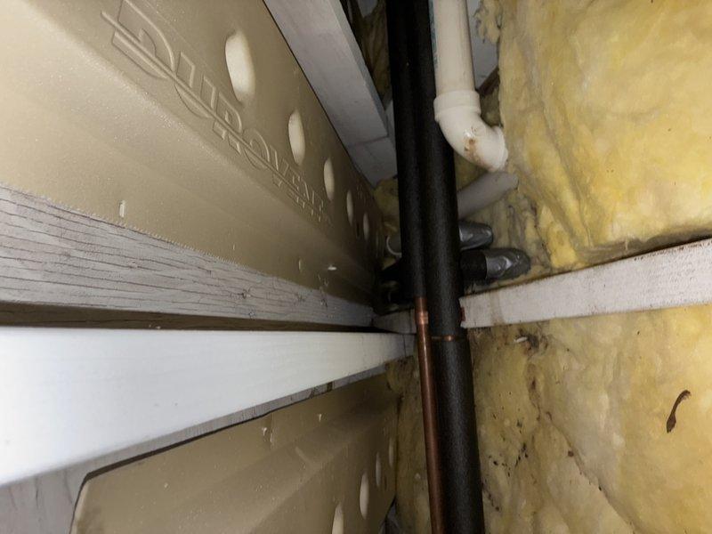 Responded to emergency call for leak investigation. Upon arrival, accessed property and proceeded with diagnostic assessment. Cut section of drywall to expose affected plumbing area and successfully identified leak source at sink connection point. Inspection revealed compromised pipe joint in utility space where copper supply lines connect to fixture. Documented conditions with photography showing vertical black pipe, copper supply line, and PVC drain system configuration. Leak originated at brass fitting connection serving sink supply. Area showed visible water damage and staining on adjacent wall surfaces. Provided assessment findings and repair recommendations to proceed with permanent correction of failed connection.