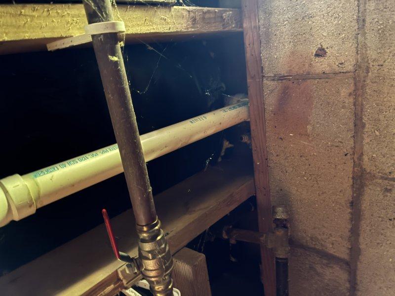Responded to emergency call for leak investigation. Upon arrival, accessed property and proceeded with diagnostic assessment. Cut section of drywall to expose affected plumbing area and successfully identified leak source at sink connection point. Inspection revealed compromised pipe joint in utility space where copper supply lines connect to fixture. Documented conditions with photography showing vertical black pipe, copper supply line, and PVC drain system configuration. Leak originated at brass fitting connection serving sink supply. Area showed visible water damage and staining on adjacent wall surfaces. Provided assessment findings and repair recommendations to proceed with permanent correction of failed connection.