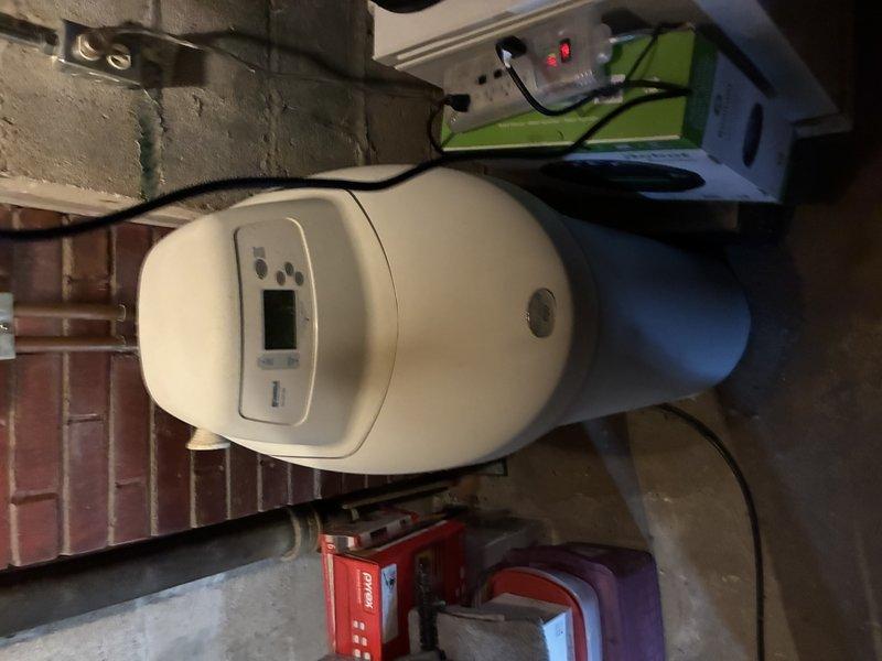 Responded to service call for water softener evaluation after unit displayed error message following 24-hour operation cycle. Upon inspection, identified existing water treatment system as over 20 years old with outdated control panel and digital display. Documented current installation configuration including copper supply line connections with brass compression fittings, red-handled shut-off valve, and PVC drain line. Assessed unit positioning in basement utility area near brick wall structure and concrete floor. Photographed existing equipment setup, plumbing connections, electrical supply with power cord to wall outlet, and overall system layout. Provided estimate for complete water softener replacement due to age of existing equipment and operational failure.