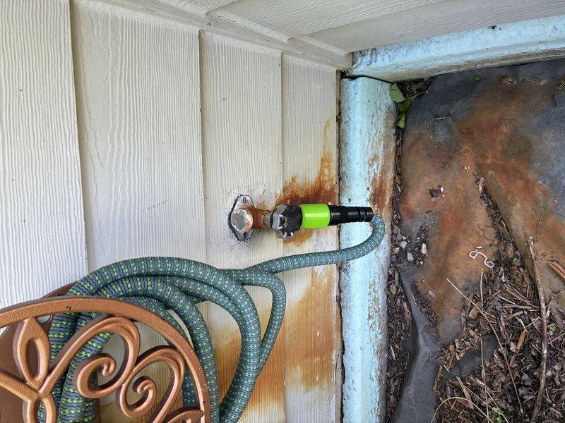 Responded to call for leaking hose bib at exterior wall junction. Upon inspection, identified active leak at outdoor spigot connection causing rust staining on white wood siding. Accessed shut-off valve from interior crawl space through attic access point. Installed new gate valve with blue handle on copper supply line to provide isolation capability for future maintenance. Tested system for proper operation and verified leak resolution at exterior hose bib connection point.