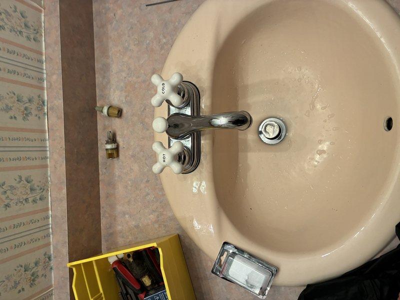 Completed faucet cartridge replacement on bathroom sink fixture with chrome finish and porcelain cross-handles. Serviced both hot and cold water cartridges, tested operation for proper flow and temperature control, and verified all connections under sink including supply lines and P-trap assembly for leaks. All components functioning properly upon completion.