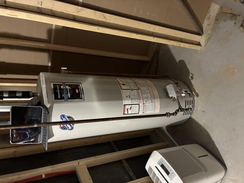 Performed on-site assessment of residential water heater located in basement utility area to provide estimate for water heater flush service. Inspected white cylindrical electric water heater unit, examined manufacturer specifications, control panel, and warning labels to determine maintenance requirements. Documented current condition of unit and surrounding mechanical equipment area through photographic documentation for estimate preparation purposes.