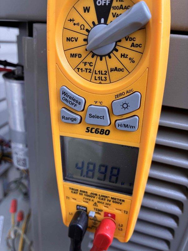 Completed annual air conditioning tune-up on outdoor condensing unit. Performed standard maintenance inspection, verified electrical readings using digital multimeter showing 4.098 microfarads capacitance within normal operating range, and confirmed system operational status. Unit accessible with adequate clearance despite nearby landscaping.
