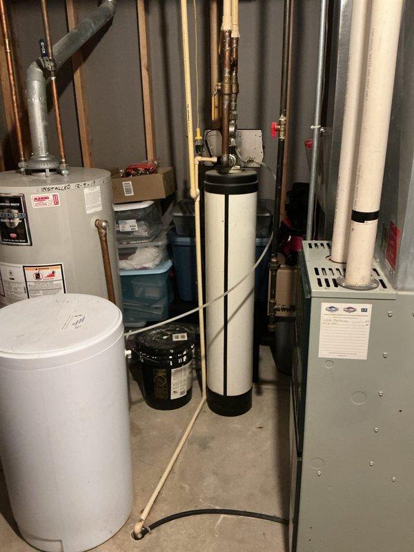 Conducted on-site evaluation of existing water softening system in basement mechanical room for replacement estimate. Assessed current water softener unit with beige control box, copper piping connections, and red-handled shut-off valves, noting configuration alongside existing water heater, HVAC equipment, and associated plumbing infrastructure. Documented equipment layout, pipe routing, and installation requirements to provide comprehensive replacement proposal for new water treatment system.
