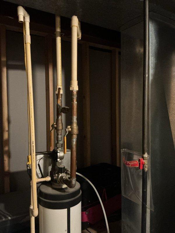 Conducted on-site evaluation of existing water softening system in basement mechanical room for replacement estimate. Assessed current water softener unit with beige control box, copper piping connections, and red-handled shut-off valves, noting configuration alongside existing water heater, HVAC equipment, and associated plumbing infrastructure. Documented equipment layout, pipe routing, and installation requirements to provide comprehensive replacement proposal for new water treatment system.