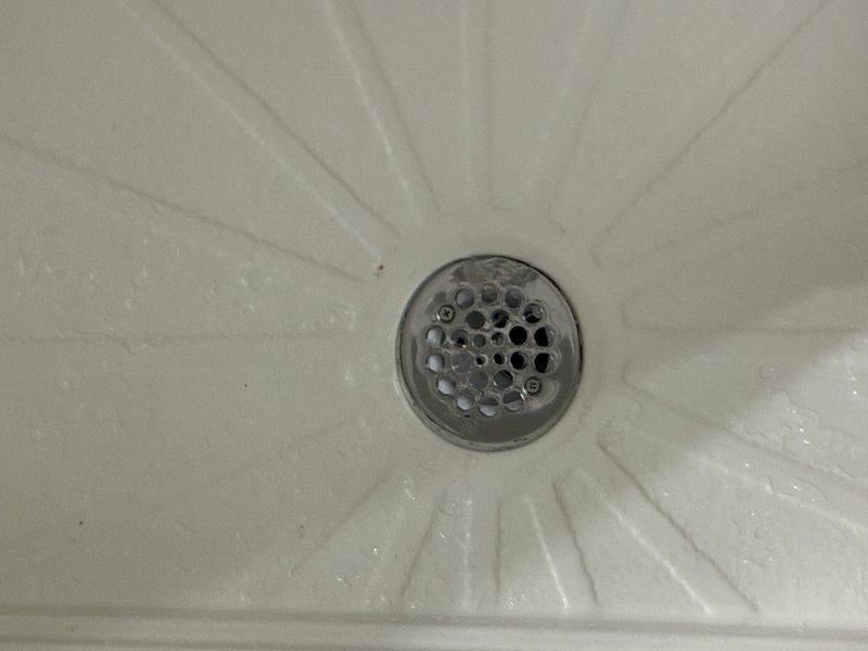 Completed shower drain replacement in residential bathroom. Accessed drain assembly through crawl space, removed existing worn drain components, and installed new white PVC drain piping with proper fittings and connections to existing waste line. Verified proper slope and secure mounting of all drain components. Tested system for leaks and confirmed proper drainage flow through basin strainer assembly.