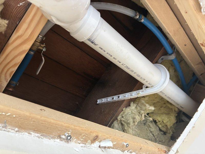 Responded to service call regarding malfunctioning outdoor hose bib with suspected pipe damage. Upon investigation, accessed interior wall cavity to expose supply line running to exterior spigot. Identified failed or damaged piping requiring replacement. Created access opening through interior wall to reach affected plumbing section. Observed existing white PVC supply line with brass fittings and blue water line running through floor/wall cavity between framing members. Assessed condition of insulation and structural framing during repair work. Documented conditions via photographs for service records.