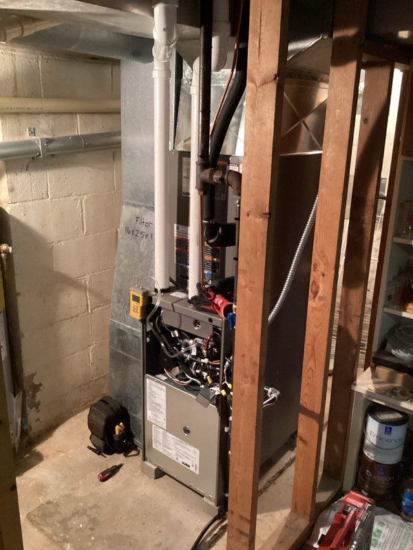 # HVAC Complete System Installation

Successfully completed full HVAC system installation in basement utility area. Installed new gray metal furnace unit with proper mounting and leveling on concrete floor. Connected white PVC vent piping running vertically for exhaust and intake air management. Installed red gas line connection with blue-handled shutoff valve for fuel supply control. Routed flexible metallic conduit for electrical connections and refrigerant lines along floor to outdoor condensing unit. Verified all internal wiring connections including red and black power leads and control circuits. Tested system operation using diagnostic equipment to confirm proper furnace ignition, blower motor function, and safety controls. Ensured proper clearances from wooden framing and stored materials per code requirements. System commissioned and operating within manufacturer specifications.