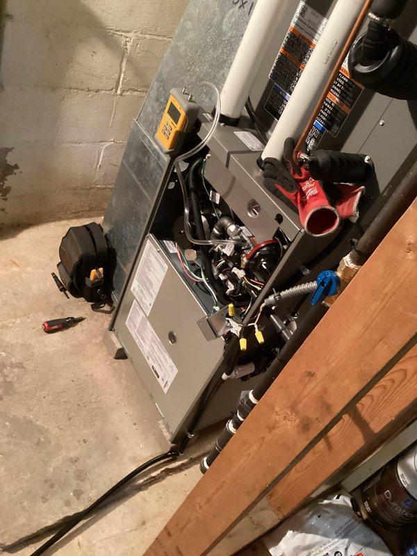 # HVAC Complete System Installation

Successfully completed full HVAC system installation in basement utility area. Installed new gray metal furnace unit with proper mounting and leveling on concrete floor. Connected white PVC vent piping running vertically for exhaust and intake air management. Installed red gas line connection with blue-handled shutoff valve for fuel supply control. Routed flexible metallic conduit for electrical connections and refrigerant lines along floor to outdoor condensing unit. Verified all internal wiring connections including red and black power leads and control circuits. Tested system operation using diagnostic equipment to confirm proper furnace ignition, blower motor function, and safety controls. Ensured proper clearances from wooden framing and stored materials per code requirements. System commissioned and operating within manufacturer specifications.